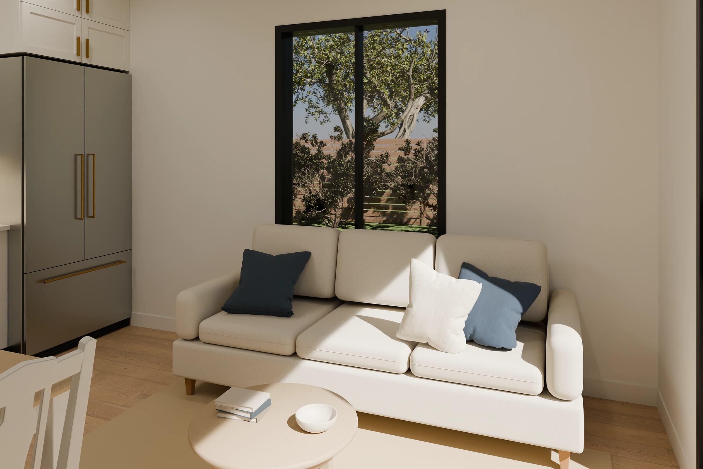 Rendering of the One Bedroom ADU living room, a cream sofa with navy and blue pillows under a tall black-framed window to the garden behind a round coffee table with books and a bowl, beside a stainless refrigerator and white shaker cabinets with brass pulls